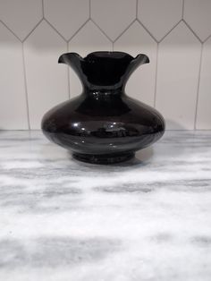 a black vase sitting on top of a marble countertop next to a white tiled wall