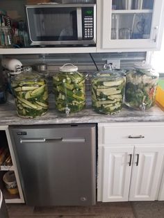 several jars filled with cucumbers sitting on top of a counter next to a dishwasher