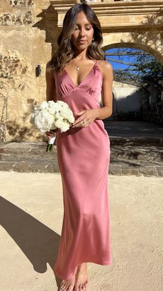 a woman in a long pink dress holding a white bouquet and posing for the camera