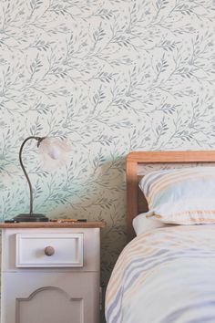 a small nightstand with a lamp on it next to a wallpapered bedroom area