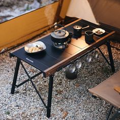 an outdoor table with food on it in the middle of gravel area next to a bench