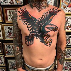 a bald man with tattoos on his chest and eagle tattoo on his upper half is standing in front of a wall full of framed pictures