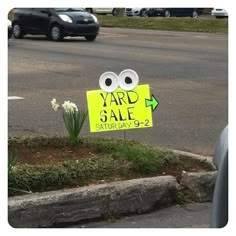 a yard sale sign sitting on the side of a road next to a flower bed