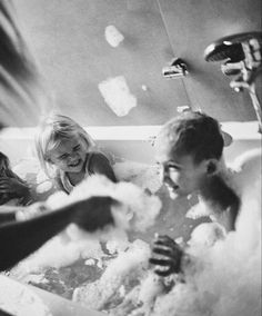 three children are playing in the bathtub with foamy bubbles and water coming out of it