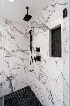 a bathroom with white marble walls and flooring, shower head and hand held shower faucet