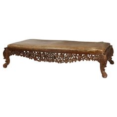 an ornate wooden bench with leather cushion on the top and legs, sitting against a white background