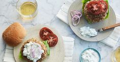 two burgers with lettuce, tomato and onion on them next to glasses of beer