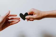 two hands reaching out towards each other holding a black heart