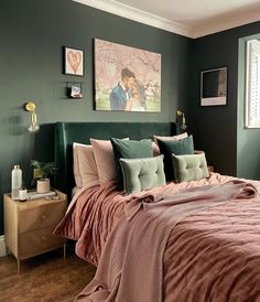 a bed with pink and green comforter in a bedroom next to a painting on the wall