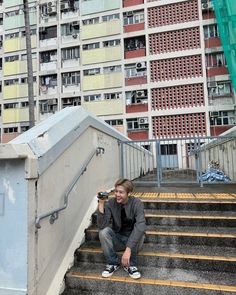 a man kneeling down on some steps in front of a building with lots of windows