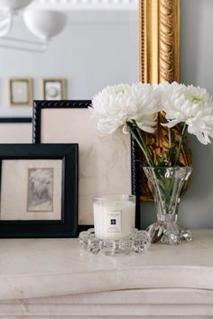 a vase filled with white flowers sitting on top of a table next to framed pictures