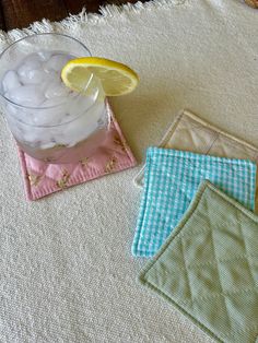 three coasters with lemon slices and ice in them on a white table cloth,