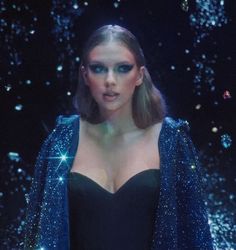 a woman in a black dress and blue jacket with sparkles on her face, standing in front of a dark background