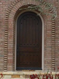 a large brown door sitting in front of a brick wall next to a planter filled with red flowers