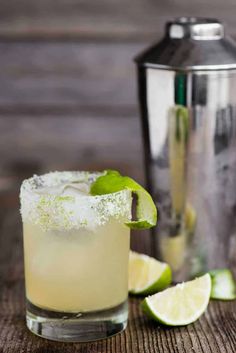 a drink with lime and sugar on the rim next to a cocktail shaker,