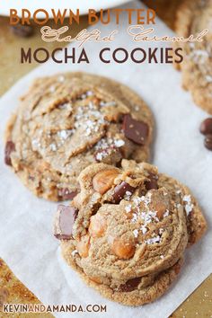 two chocolate chip cookies sitting on top of a piece of paper next to some nuts