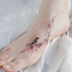 a small bird on a branch tattoo on the left foot, with pink flowers around it