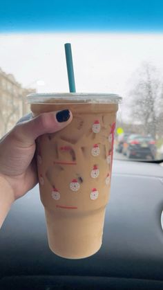 a person holding up a cup with a straw in it on the dashboard of a car