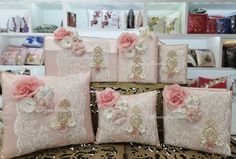 four pink pillows with flowers on them sitting on a table in front of bookshelves