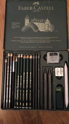 an assortment of pencils and crayons in a black box on a wooden table