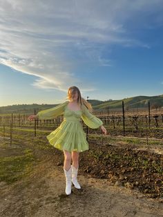 a woman in a green dress and white socks standing on a dirt road with her arms outstretched