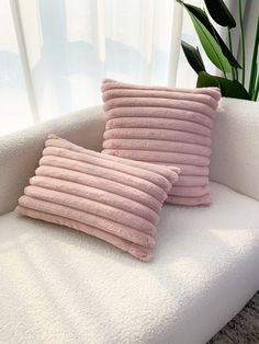 two pink pillows sitting on top of a white couch next to a potted plant