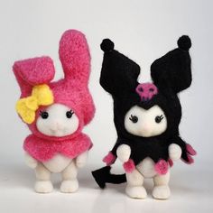 two small stuffed animals standing next to each other on a white surface with one wearing a pink and black outfit