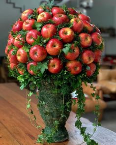 a vase filled with lots of red apples on top of a wooden table