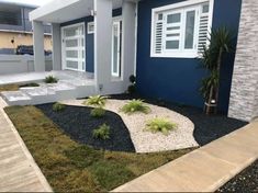 a blue house with white shutters and plants in the front yard on a sunny day