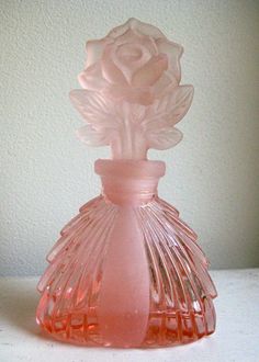 a pink glass vase with a rose on the top is sitting on a table next to a white wall