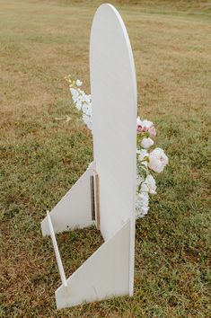 a white surfboard sitting on top of a grass covered field next to some flowers