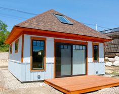 a small white and orange building with a wooden deck in front of it on gravel