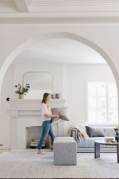 a woman walking through a living room with a fireplace and couch in front of her