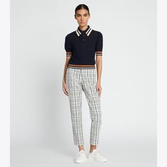 a woman standing in front of a white wall wearing plaid pants and a polo shirt