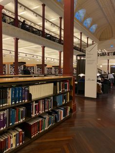 a library filled with lots of books and people sitting at tables next to it on top of hard wood flooring