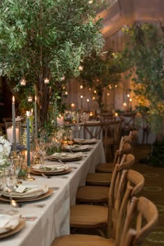 a long table set with place settings and candles in the center is surrounded by greenery