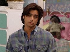 a young man standing in front of a bed with a teddy bear on the wall