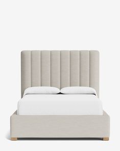 an upholstered bed with white sheets and pillows