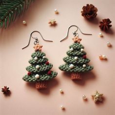 crochet christmas tree earrings on pink background with pine cone and star decorations around them