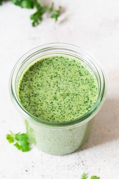 a jar filled with green liquid sitting on top of a white counter next to parsley