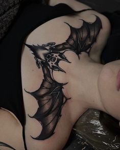 a woman laying down with a tattoo on her arm and shoulder that looks like a bat