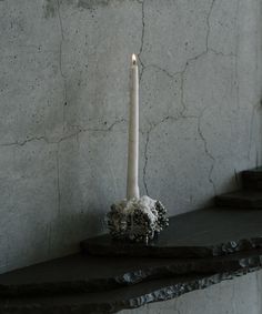 a white candle sitting on top of a black shelf next to a wall with cracks in it