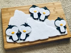 three decorated penguins sitting on top of a wooden cutting board next to a pile of carpet