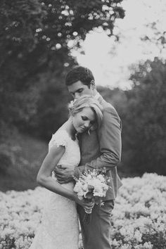 black and white photo of bride and groom in field of flowers with trees behind them