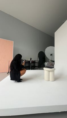 a woman sitting on top of a white counter next to a table with a mirror