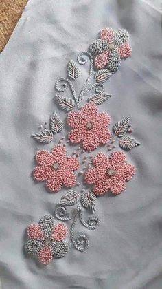 some pink flowers and leaves on a light blue shirt with silver thread work, in the shape of beads