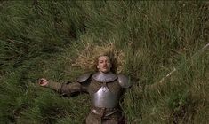 a woman dressed in armor is laying on the ground with her arms outstretched and eyes closed