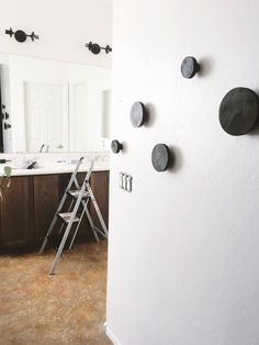 a ladder leaning against a white wall with black knobs on it and two sinks in the background