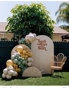 there is a sign with balloons on it in the grass next to a chair and table