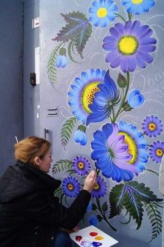 a woman painting flowers on a wall with acrylic paint and watercolors